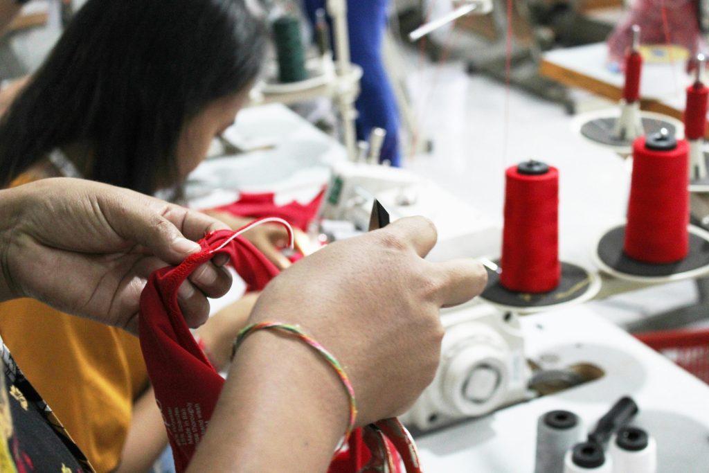 About Close-up of hands working with fabric in a sewing workshop, surrounded by spools and machinery.